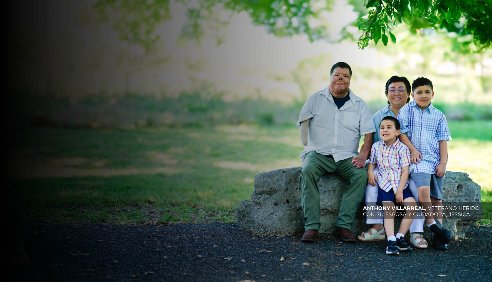 El guerrero Anthony Villarreal está sentado con su esposa y sus dos hijos bajo un árbol. Tiene cicatrices de quemaduras y le amputaron el brazo derecho por debajo del codo.